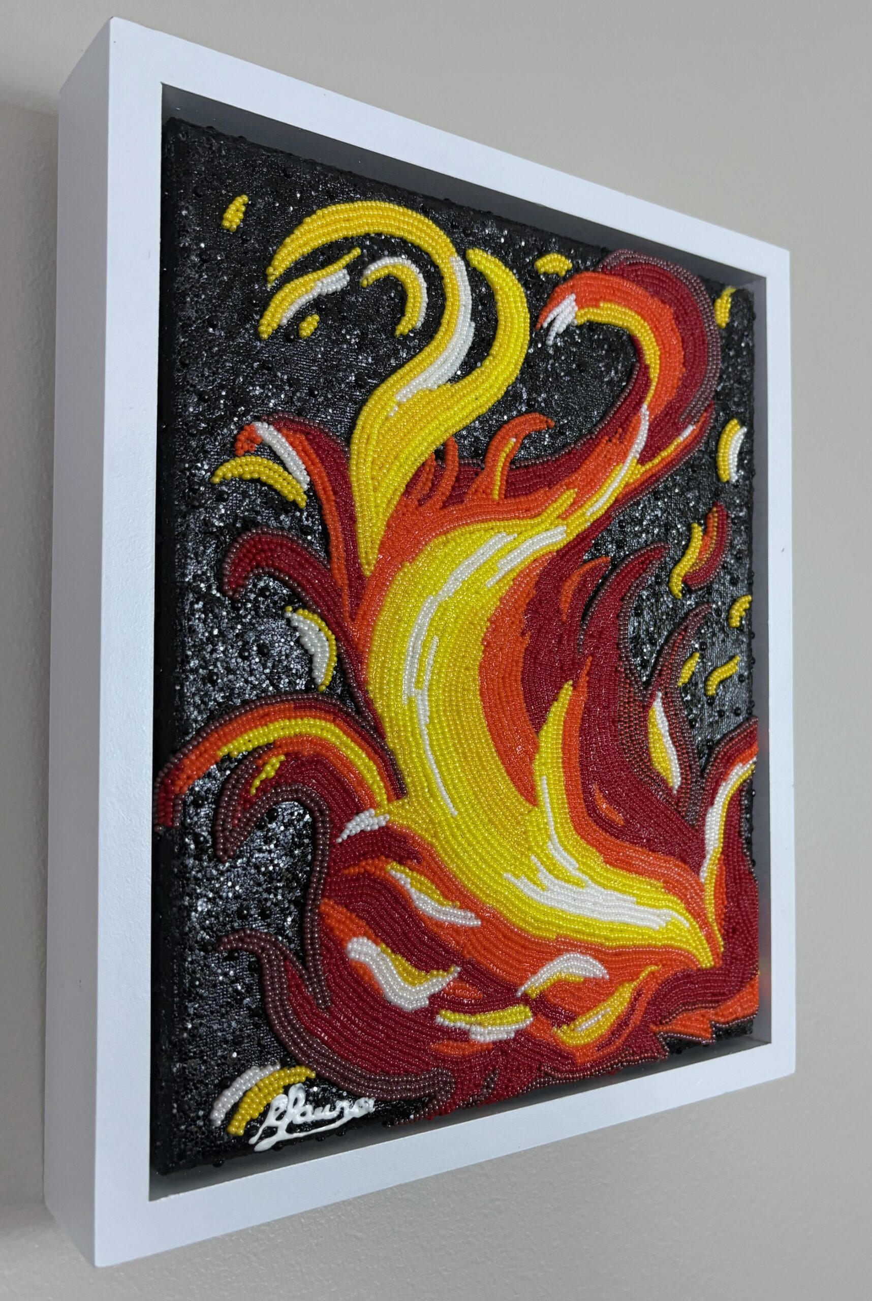 yellow, and white glass beads form expressive flames against a black painted background in Fire, a small bead mosaic in a white frame.
